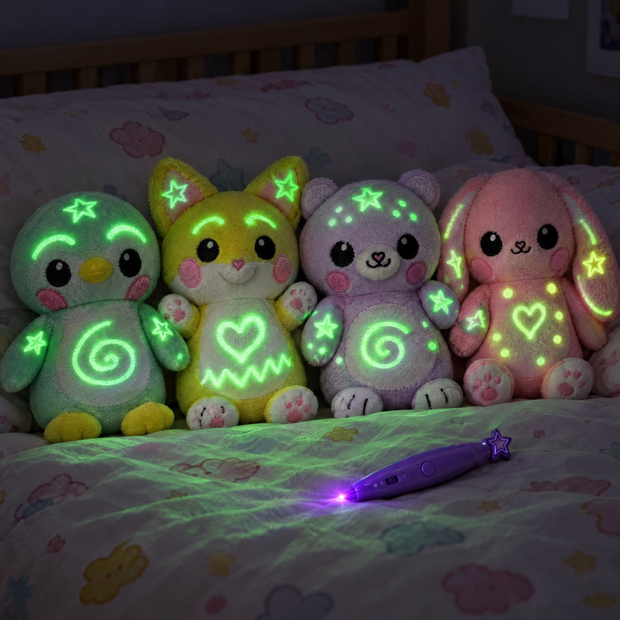 Four Glow Doodles plushies, a penguin, fox, bear and bunny, glowing with green doodles on a bed at night next to the purple light pen